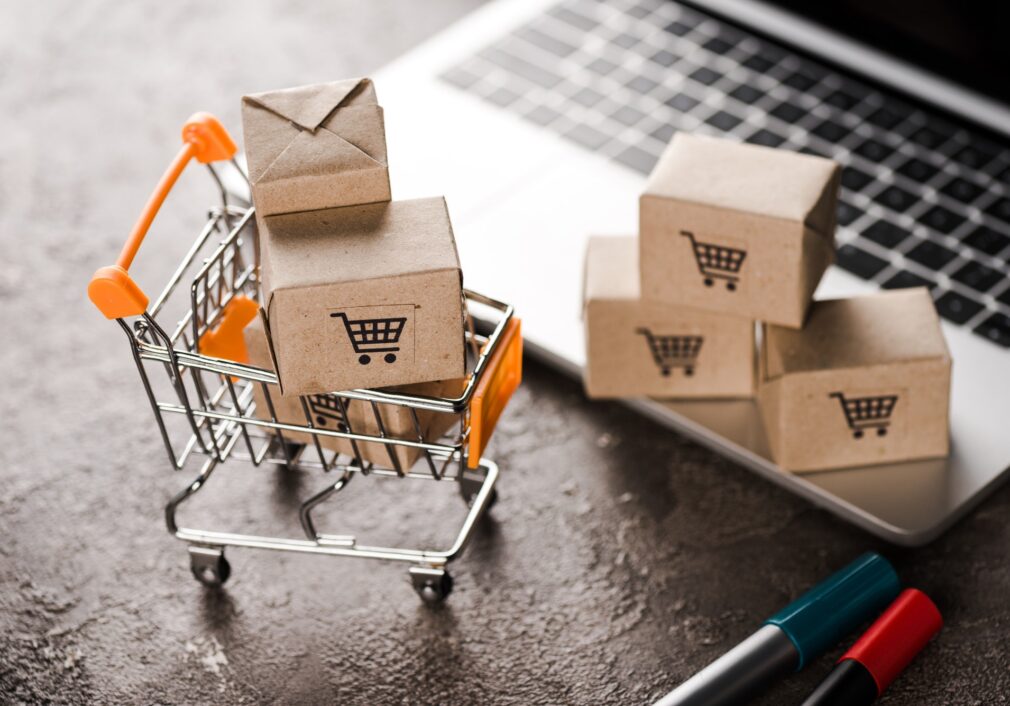 selective-focus-of-toy-shopping-cart-with-small-carton-boxes-near-laptop-e-commerce-concept