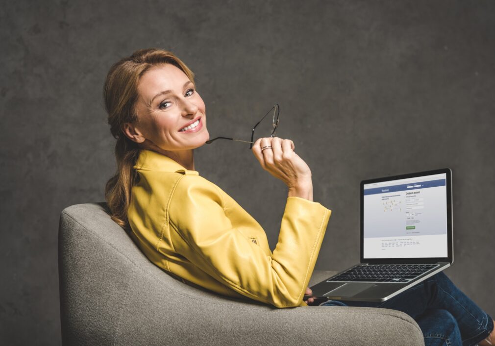 smiling-mature-woman-using-laptop-with-facebook-website-and-sitting-in-armchair